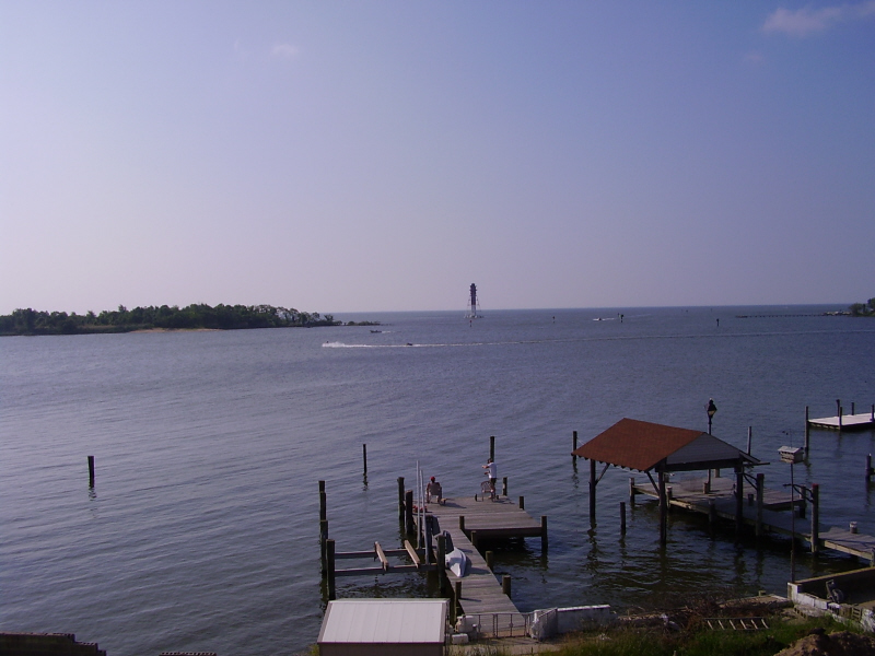 Calm bay with docks and a distant lighthouse on a clear day.