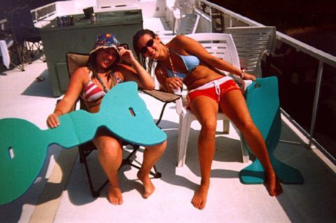 1982 Ford Bronco - Two women enjoy a sunny day on a boat, each holding a large, teal pool float shaped like a sea creature.