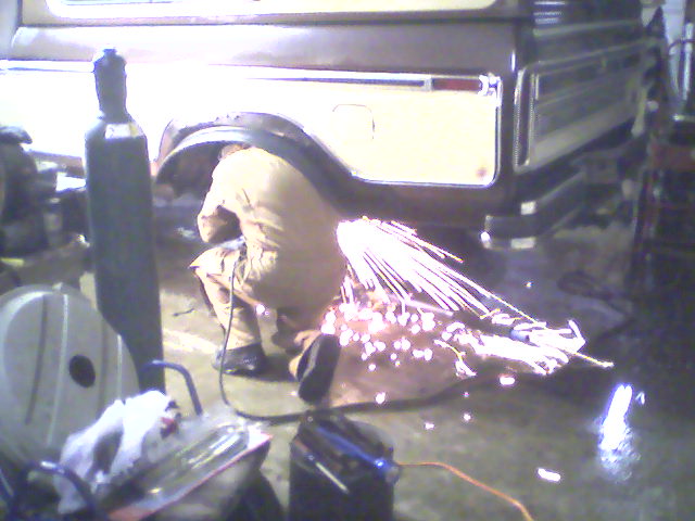 Person crouched welding under the rear of a vehicle with sparks flying in a garage
