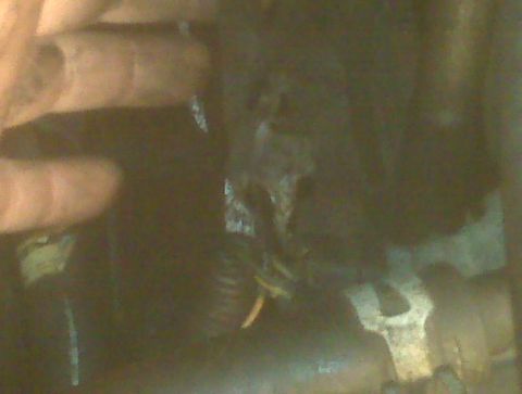 1995 Ford Bronco - A close-up view of a hand reaching towards a bundle of wires and a metal bracket, possibly in an engine bay.