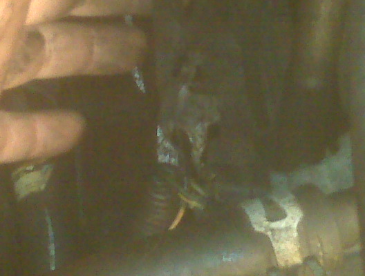 Hand reaching towards wires and metal bracket in engine bay