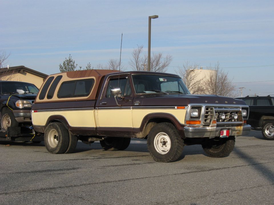 Brown and tan 1978 Ford pickup with camper shell parked in a lot