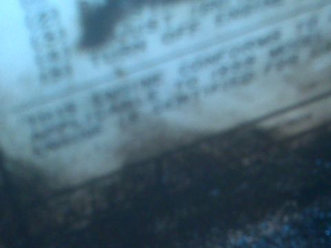 1995 Ford Bronco - A close-up, blurry shot shows a document with text, possibly a vehicle identification sticker or manual page, with a dark, textured surface…