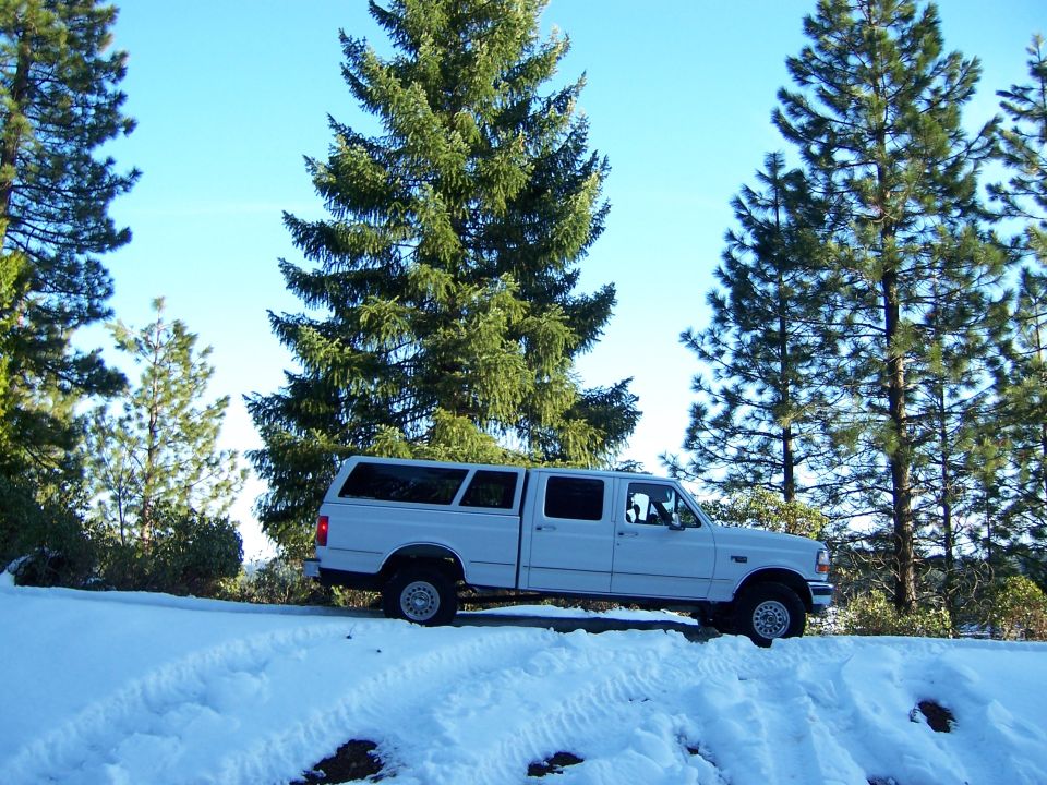 Photo of a white truck with camper shell parked in the snow