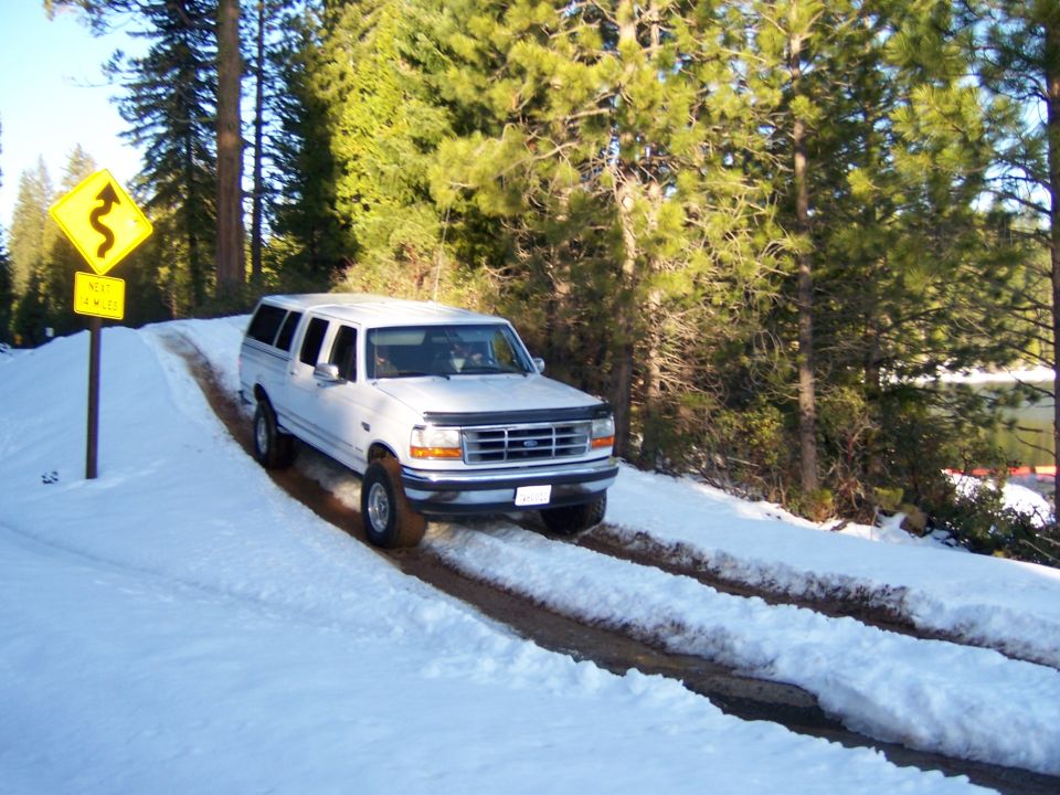 Photo of a white truck on a plowed snowy road past a curve sign