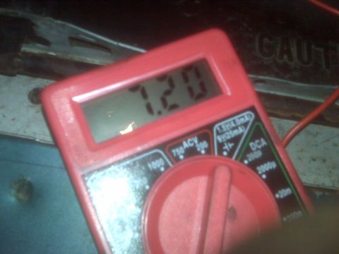 1995 Ford Bronco - A red digital multimeter displays a reading of 7.20, positioned in front of a dark, possibly metallic surface with the word "CAUTION" visib…