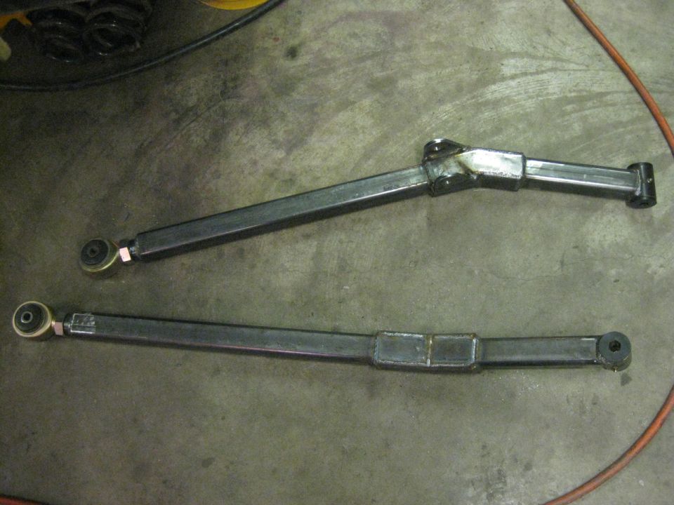 Two custom steel control arms on concrete floor