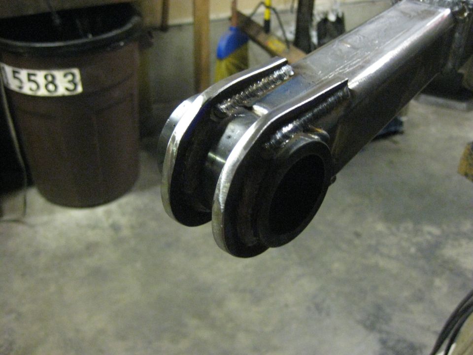 Close-up of welded metal part, possibly for a vehicle, with a trash can in the background.