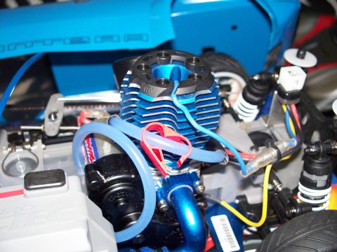 1990 Ford Bronco - Close-up view of a blue and black nitro engine with blue fuel lines and a red clip. The engine is part of a vehicle's mechanical assembly.