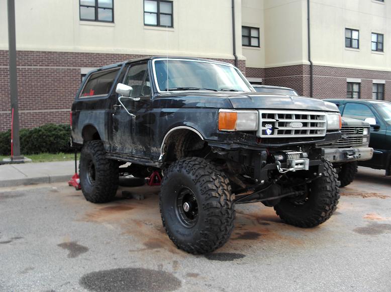 Lifted black 1990 Ford Bronco with large off-road tires and a winch.