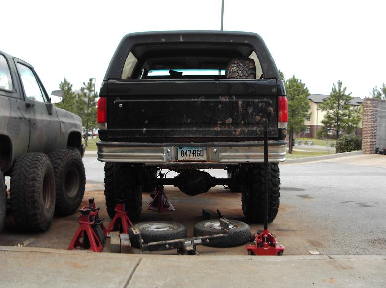 Black Ford Bronco lifted on jack stands with rear tires removed, spare tire visible inside.