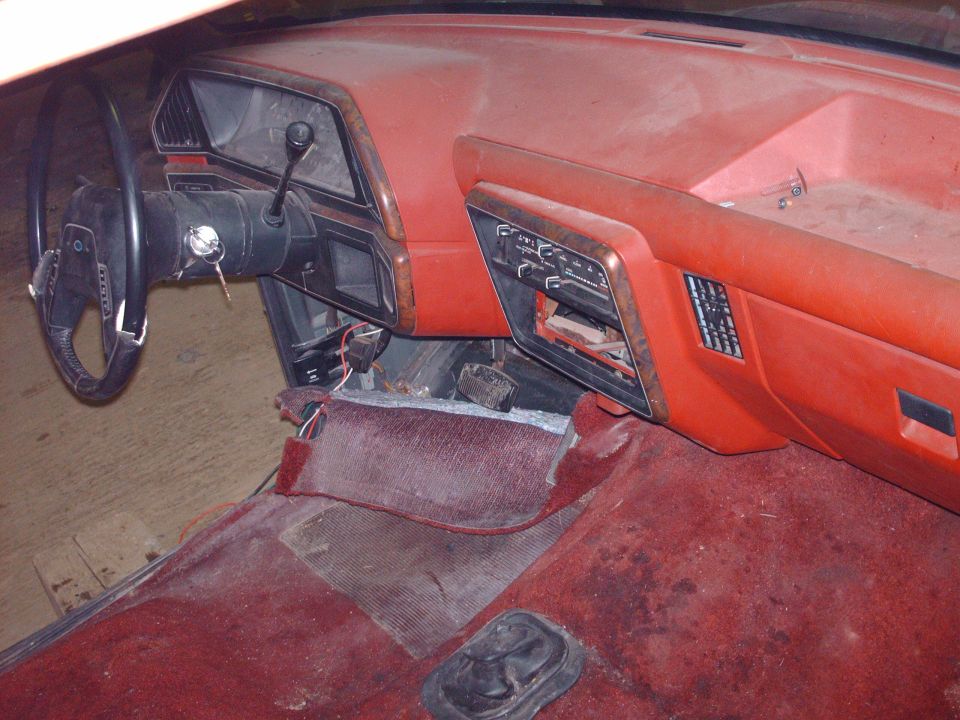 Dusty red car interior dashboard with steering wheel, radio, and floor mats.
