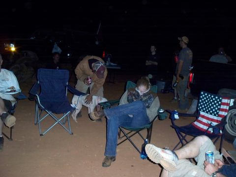 1996 Ford Bronco - A group of people are gathered around vehicles at night, some relaxing in chairs while others stand.