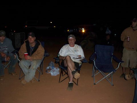 1996 Ford Bronco - Several men are gathered outdoors at night, seated in camping chairs with vehicles in the background.