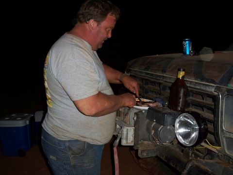 1996 Ford Bronco - A man prepares to eat meat from a plate while standing next to a vehicle at night.