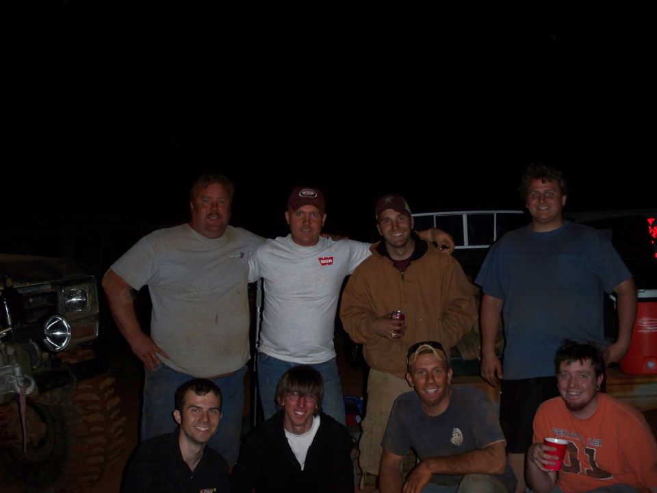 group of men posing for a photo at night, with a vehicle partially visible on the left
