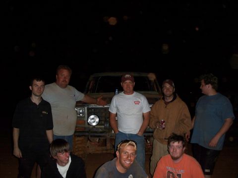 1996 Ford Bronco - Men pose for a photo in front of a muddy truck at an outdoor event.