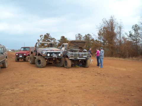 1996 Ford Bronco - Modified trucks gathered on a dirt area, with people and a dog observing.