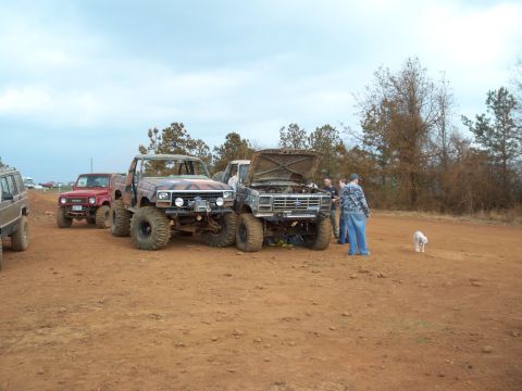 1996 Ford Bronco - Several off-road vehicles are gathered on a dirt lot under a cloudy sky.
