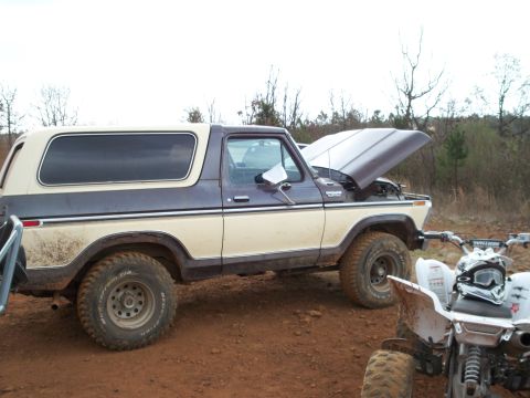 1996 Ford Bronco - Ford Bronco and an ATV parked on dirt ground, with trees in the background.
