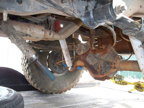1996 Ford Bronco - Close-up of a vehicle's rusty rear axle and suspension components, with a yellow Allied strap securing it.