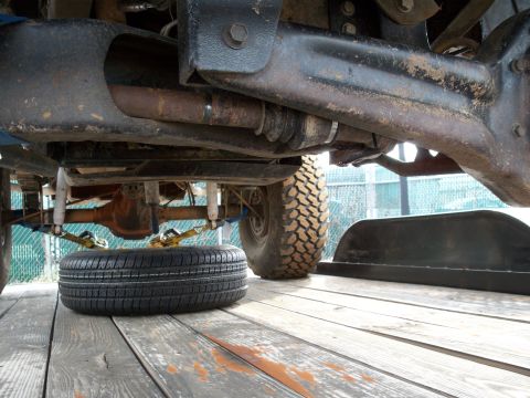 1996 Ford Bronco - A low-angle shot reveals the undercarriage of a vehicle, including its suspension and a spare tire secured on a wooden surface.
