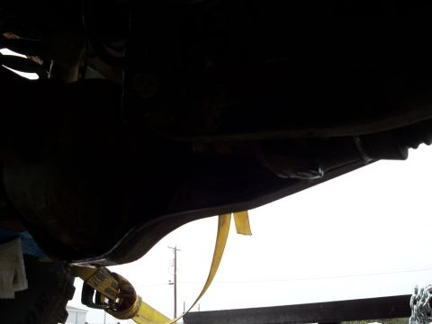 1996 Ford Bronco - The underside of a vehicle is captured from a low angle, showing mechanical components and a yellow strap.