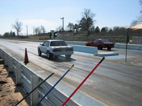1992 Ford Mustang - A white 1992 Ford Mustang competes on a drag strip alongside another vehicle under a clear sky.