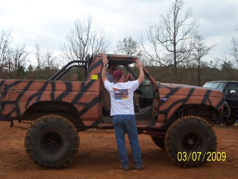 1996 Ford Bronco - A modified Ford Bronco with custom paint sits in a dirt lot with two people nearby.
