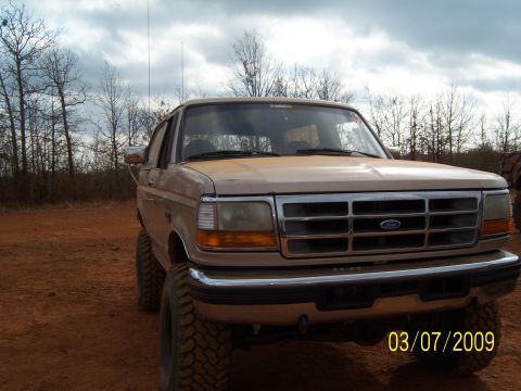 1996 Ford Bronco - A tan Ford truck is parked outdoors on a dirt road under a cloudy sky.