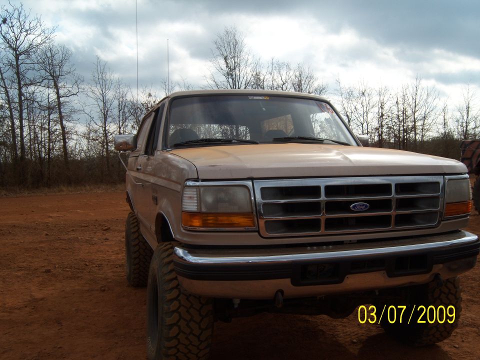 Tan Ford truck with lifted suspension and large tires, front view