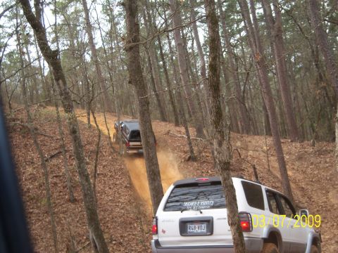 1996 Ford Bronco - Two SUVs navigate a wooded trail on a dirt path.
