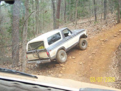 1996 Ford Bronco - A two-tone Ford Bronco navigates a rocky, wooded trail on a sunny day.