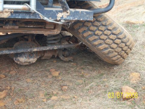 1996 Ford Bronco - Close-up of a muddy rear axle and tire of an off-road vehicle on dry, rocky ground.