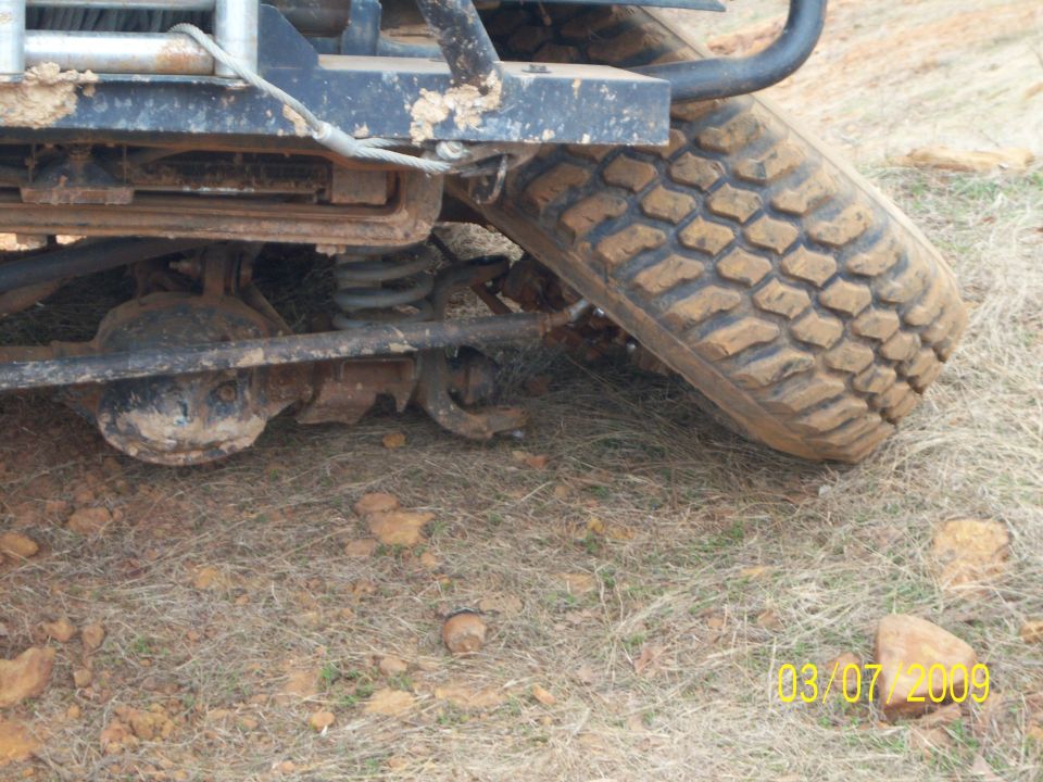 Mud-covered off-road vehicle rear axle and tire on dry grass