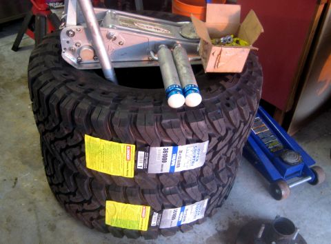 1996 Ford Bronco - Automotive parts including tires, shock absorbers, and a floor jack are arranged on a concrete floor.