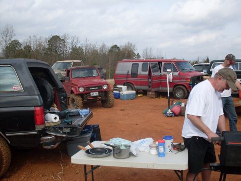 1996 Ford Bronco - Several off-road vehicles are parked at a campsite with a table set up for cooking.