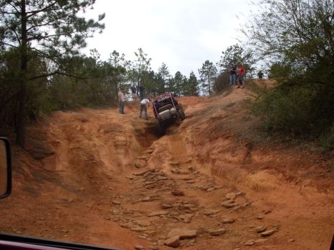 1996 Ford Bronco - An off-road vehicle descends a challenging dirt and rock path with onlookers observing the difficult maneuver.