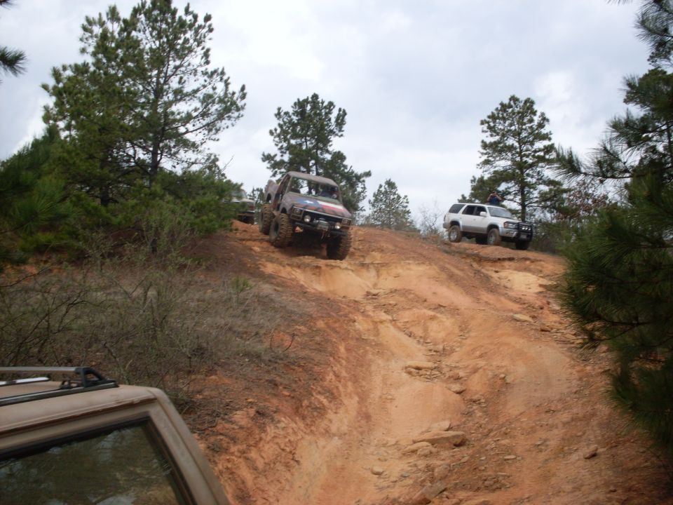 off-road vehicles climbing a steep dirt hill with trees around