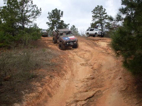 1996 Ford Bronco - Multiple off-road vehicles navigate a steep, rocky incline on a dirt trail under a cloudy sky.