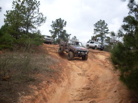 1996 Ford Bronco - Several off-road vehicles navigate a challenging dirt incline, with a 1996 Ford Bronco leading the ascent.