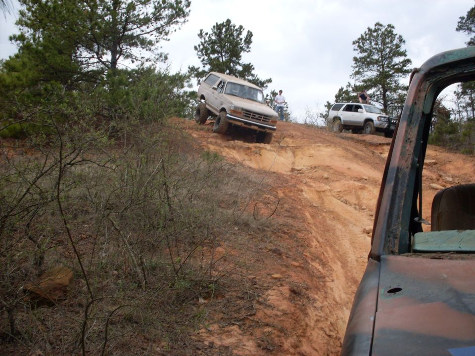 1996 Ford Bronco climbing a steep dirt hill, with another SUV and part of a third vehicle visible