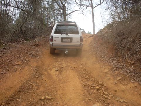 1996 Ford Bronco - White SUV navigates a dirt trail, kicking up dust as it ascends the incline.