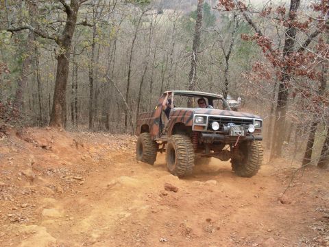 1996 Ford Bronco - Modified pickup truck with large tires navigating a dirt trail through a wooded area.