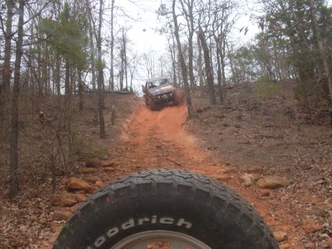 1996 Ford Bronco - Two off-road vehicles navigate a challenging dirt trail through a forest.