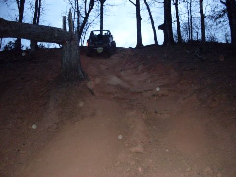 1996 Ford Bronco - A vehicle navigates a challenging dirt incline surrounded by a forest.