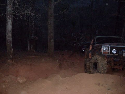 1996 Ford Bronco - An off-road vehicle navigates a dirt path through a wooded area at night.