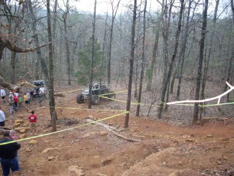 1996 Ford Bronco - An off-road buggy is driven through a wooded area marked with yellow caution tape, while onlookers observe the event.