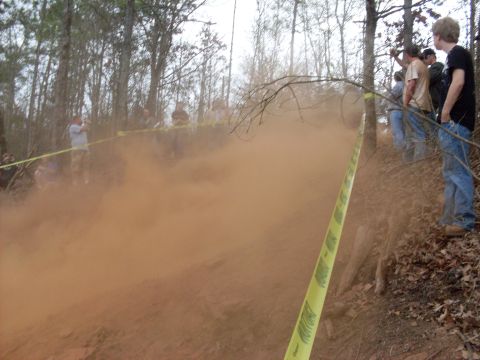 1996 Ford Bronco - An off-road vehicle creates a massive dust cloud during an event, observed by onlookers.