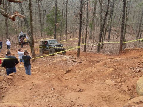 1996 Ford Bronco - Off-road vehicles traverse a challenging course marked with yellow caution tape in a wooded area.
